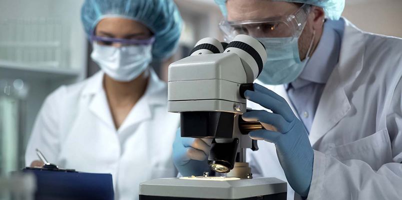 male scientists in protective covering using a microscope